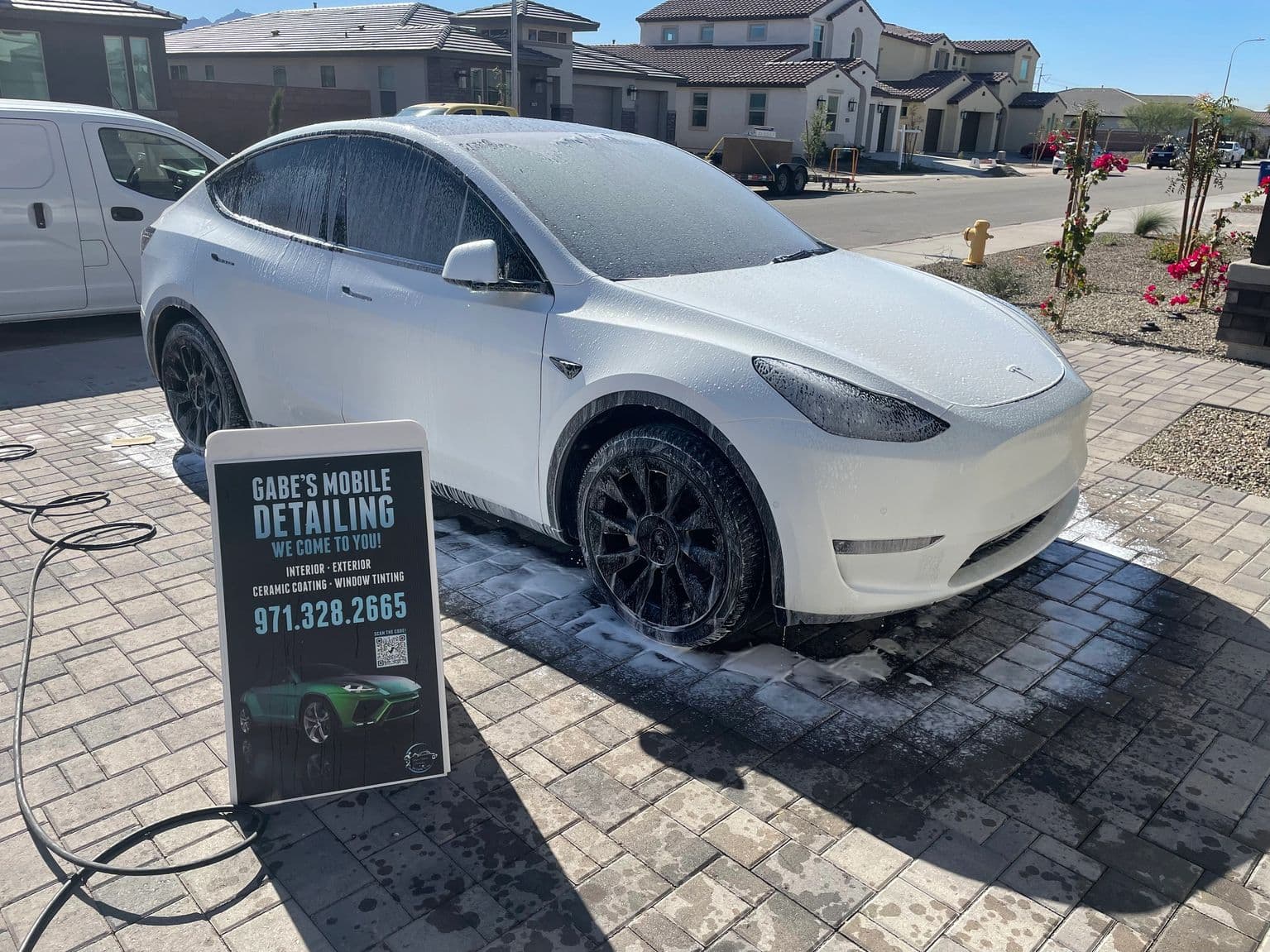 Gabe's Mobile Detailing washing a foamed-up Tesla on location in a Phoenix driveway, branded yard sign beside it